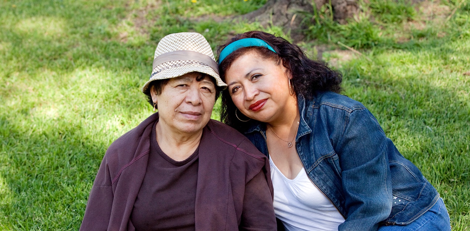 Latina mother and daughter sit side-by-side on a lawn