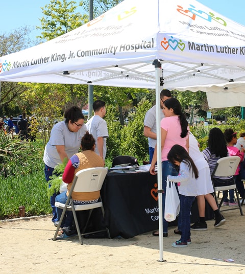 South LA community members sitting under pop up tent and speaking to community health workers 