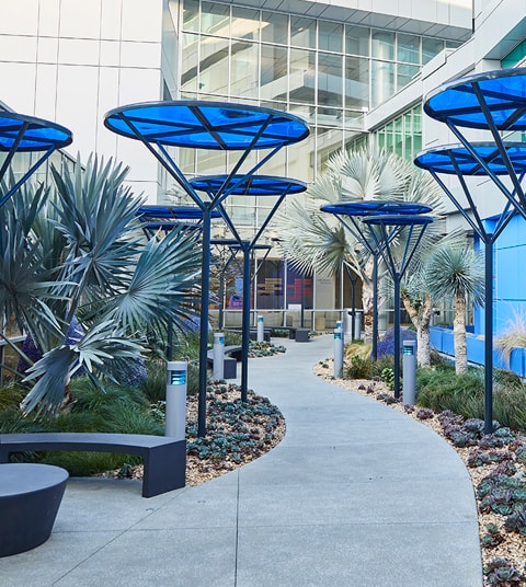 Cubiertas altas de sombra color azul que delimitan los pasillos del jardín de curación del hospital