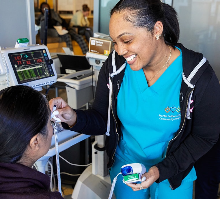 Smiling MLKCH nurse takes a patient's temperature