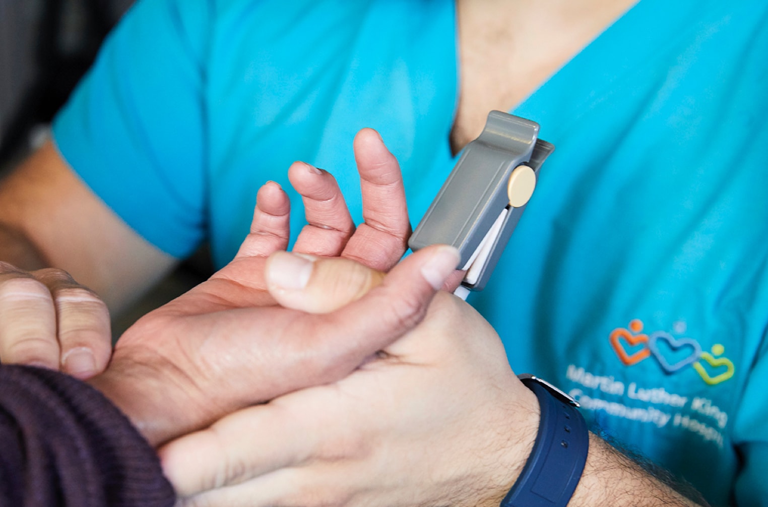 Closeup of a MLKCH nurse putting a blood pressure monitor on a man's finger