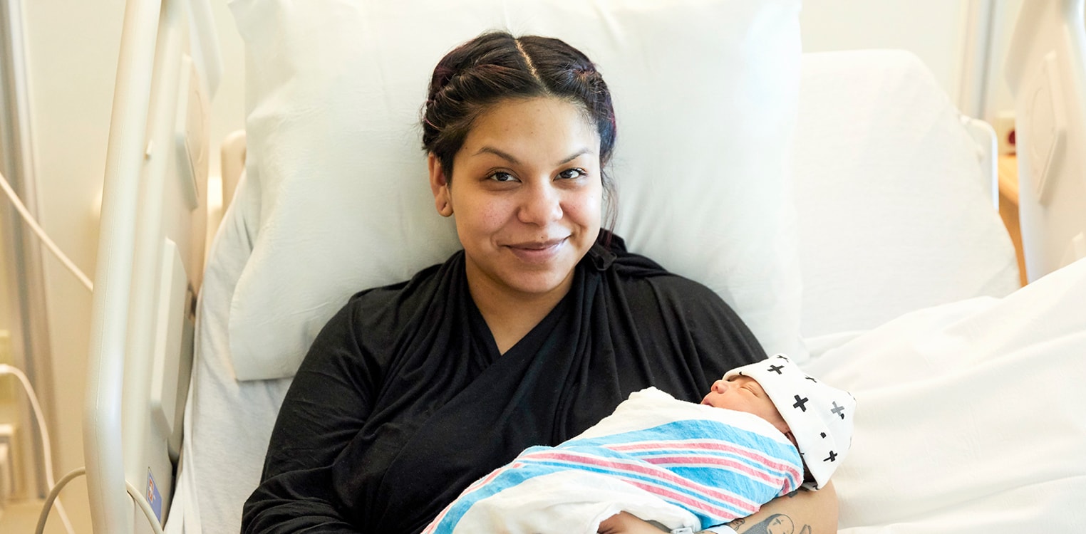 Smiling Latina mom in a hospital bed holding her newborn baby