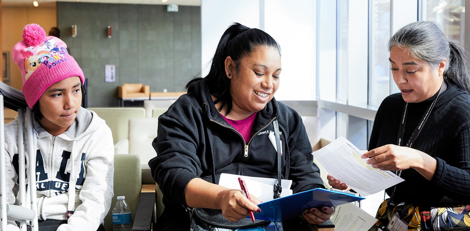 A female hospital employee reviews paperwork with a Latina woman in the waiting area