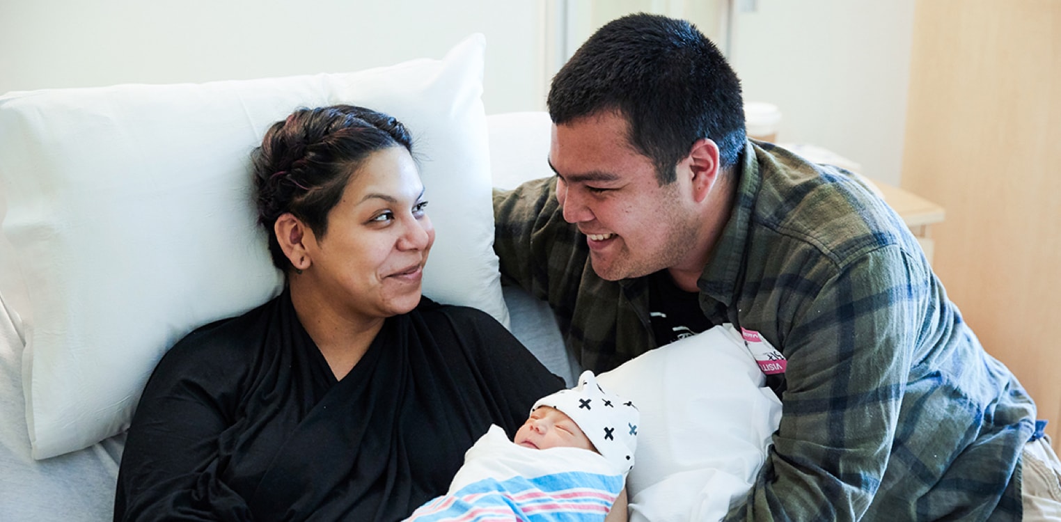 New Latino parents smile while holding their newborn baby
