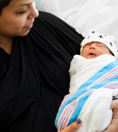 Smiling Latina mom holding and looking at her newborn baby wrapped in a blanket