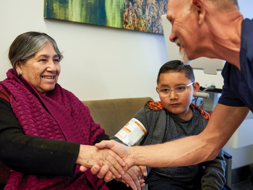White male nurse shaking an elderly Latina woman's hand in the waiting room as young boy looks on