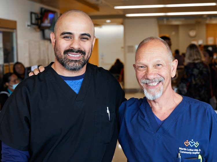 Two male nurses wearing blue scrubs smiling