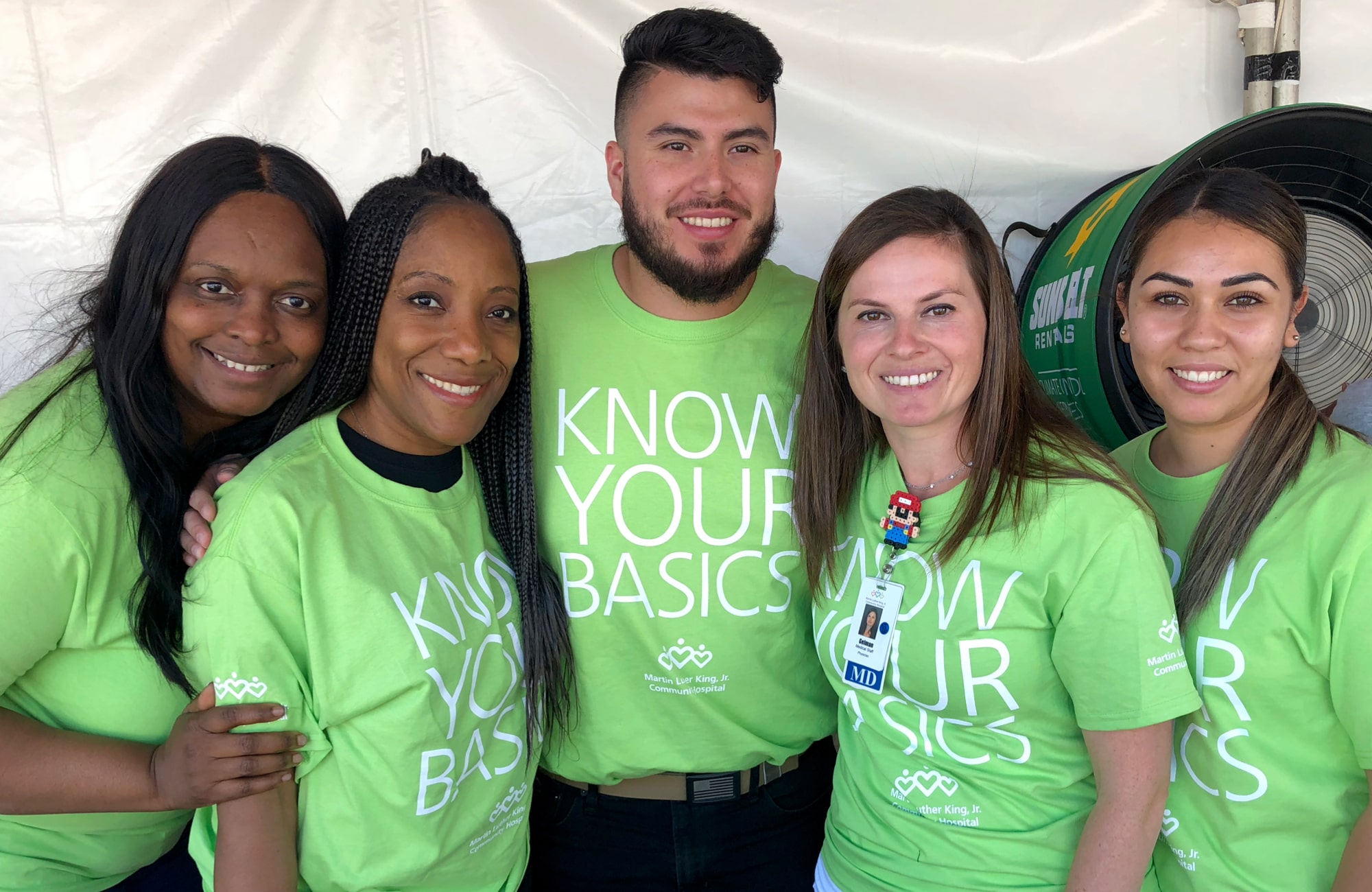 Four women and one woman of different races smiling and wearing green Know Your Basics shirts