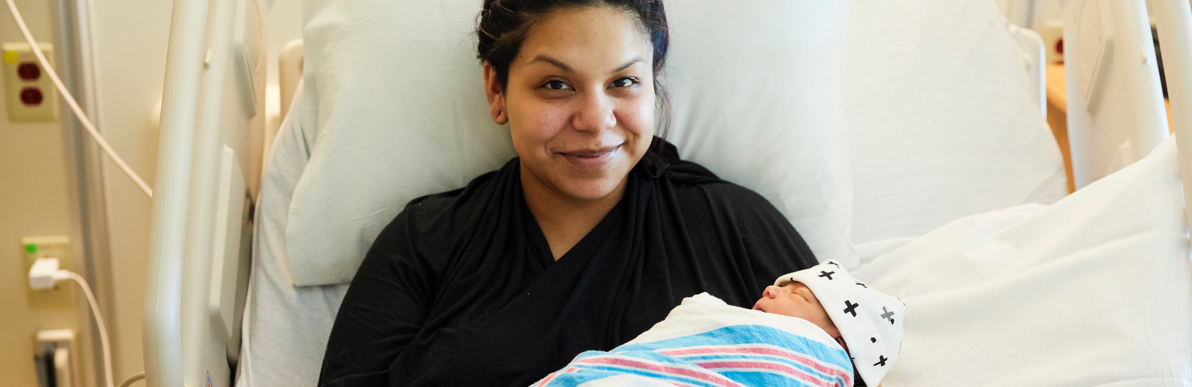Smiling Latina mom in a hospital bed holding her newborn baby
