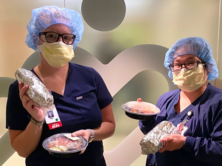 Two nurses holding up food donations
