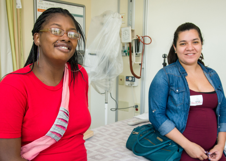Mujer de color y mujer latina sonriendo mientras hacen un recorrido por el hospital
