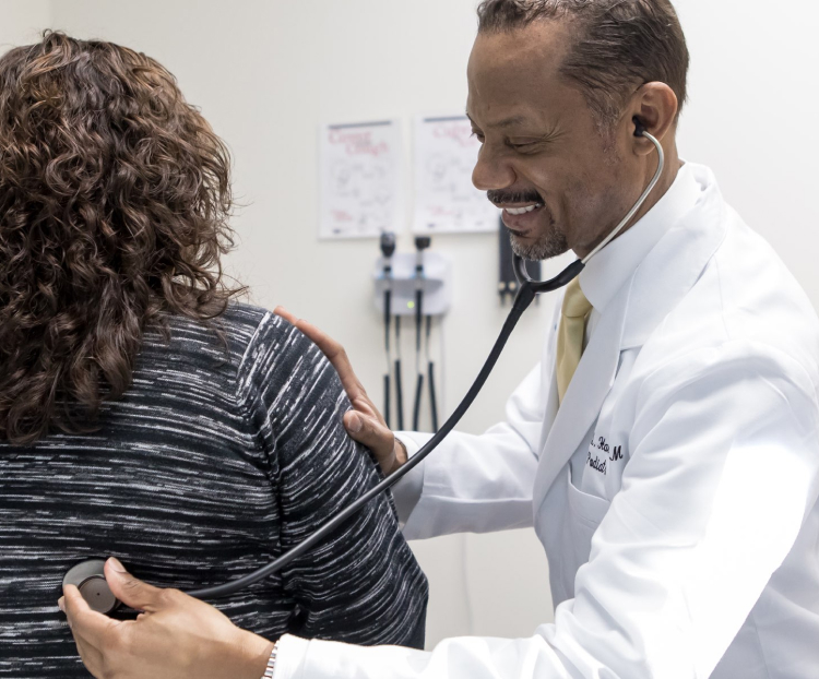 Black male doctor using stethoscope on back of female patient