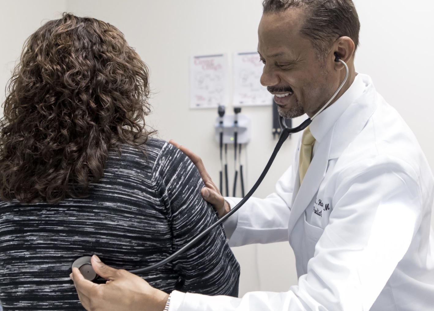 Black male doctor uses stethoscope on female patient's back