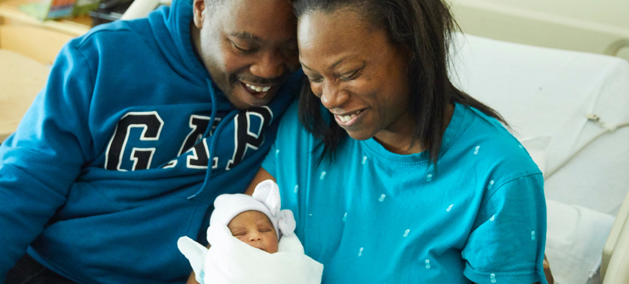 Black mother and father smiling down at swaddled newborn