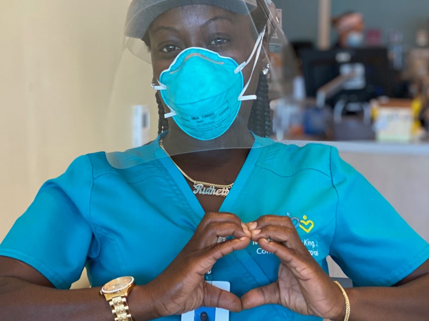 Black female nurse wearing a mask making a heart with her hands