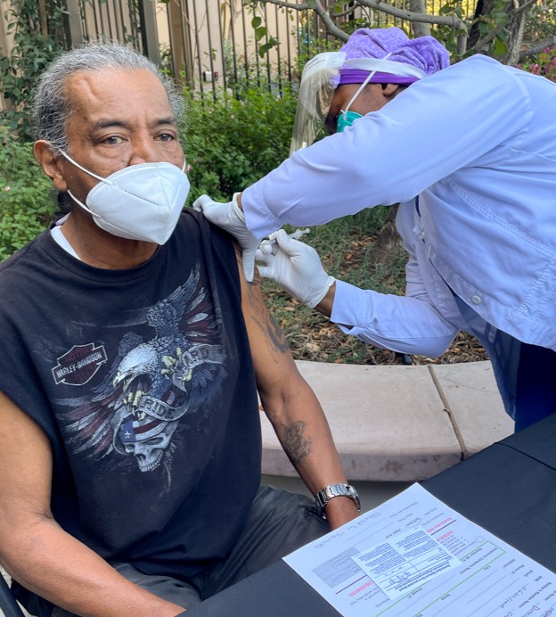 An older Black man receives a vaccination from a Black female nurse