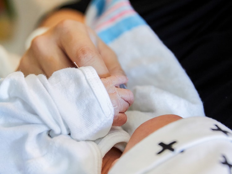 Closeup of newborn baby grasping a finger