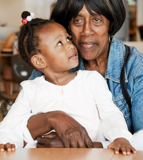 Older Black woman holding young Black girl in her lap