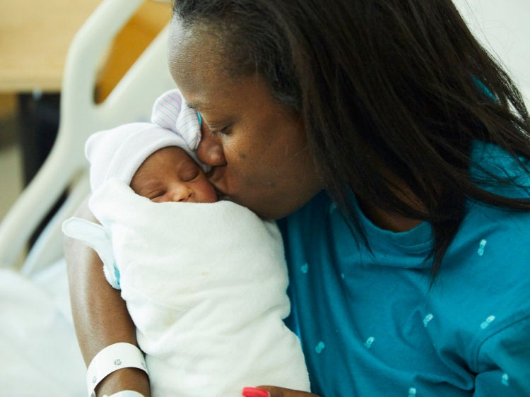 Black mother kissing swaddled newborn child