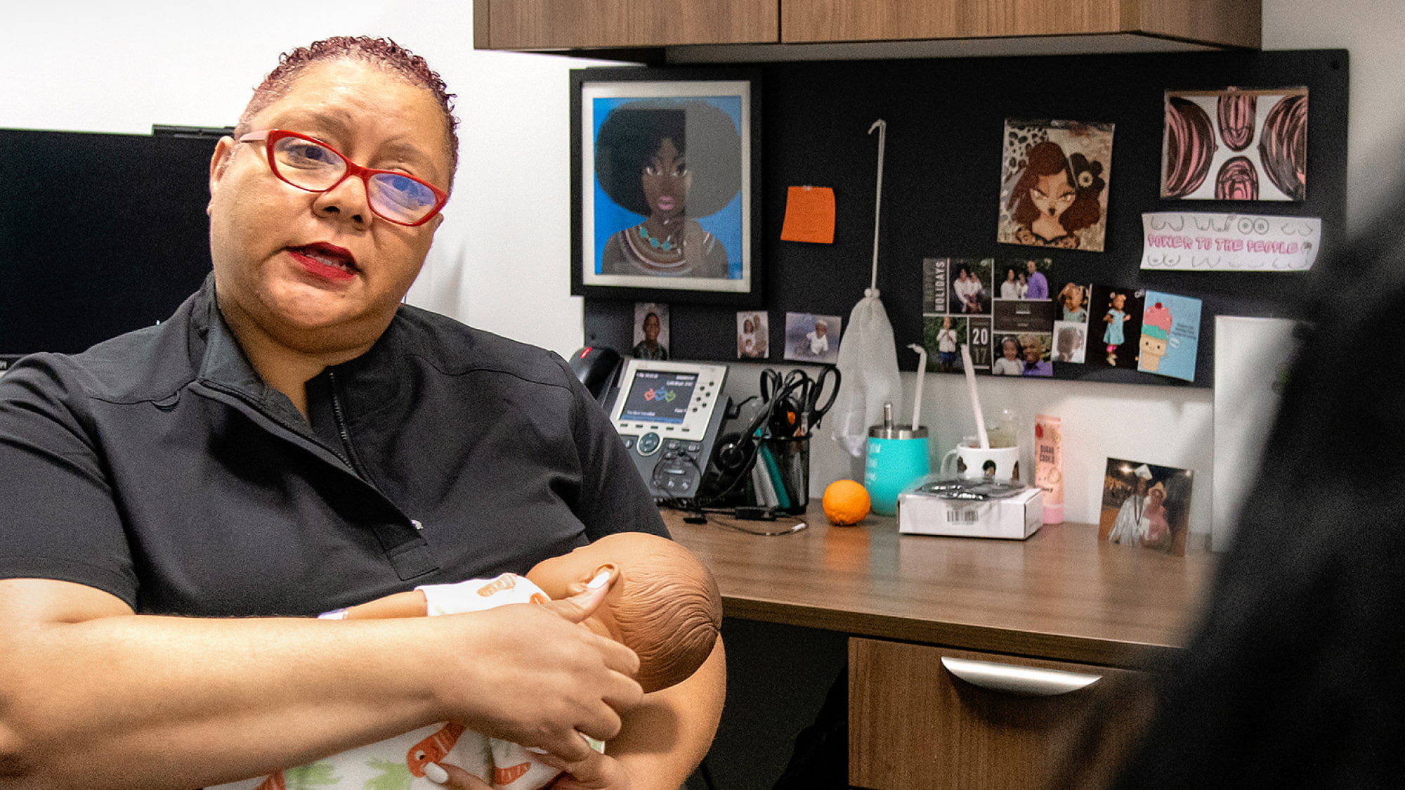 Lydia Boyd sosteniendo un bebé de utilería en su regazo frente a su escritorio