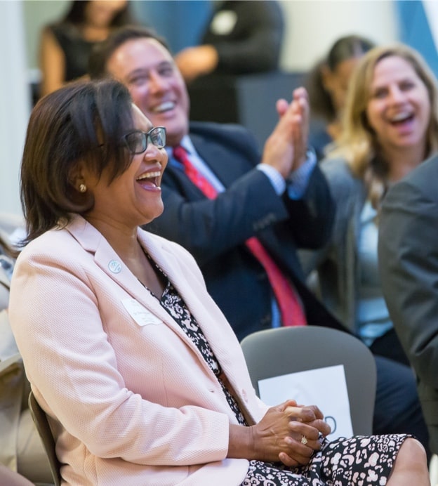 Dr. Batchlor, a middle-aged Black woman, sitting at donor wall dedication and laughing