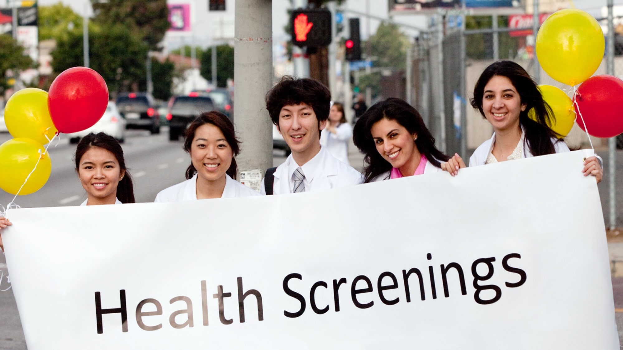 Five people holding a white banner that reads health screenings