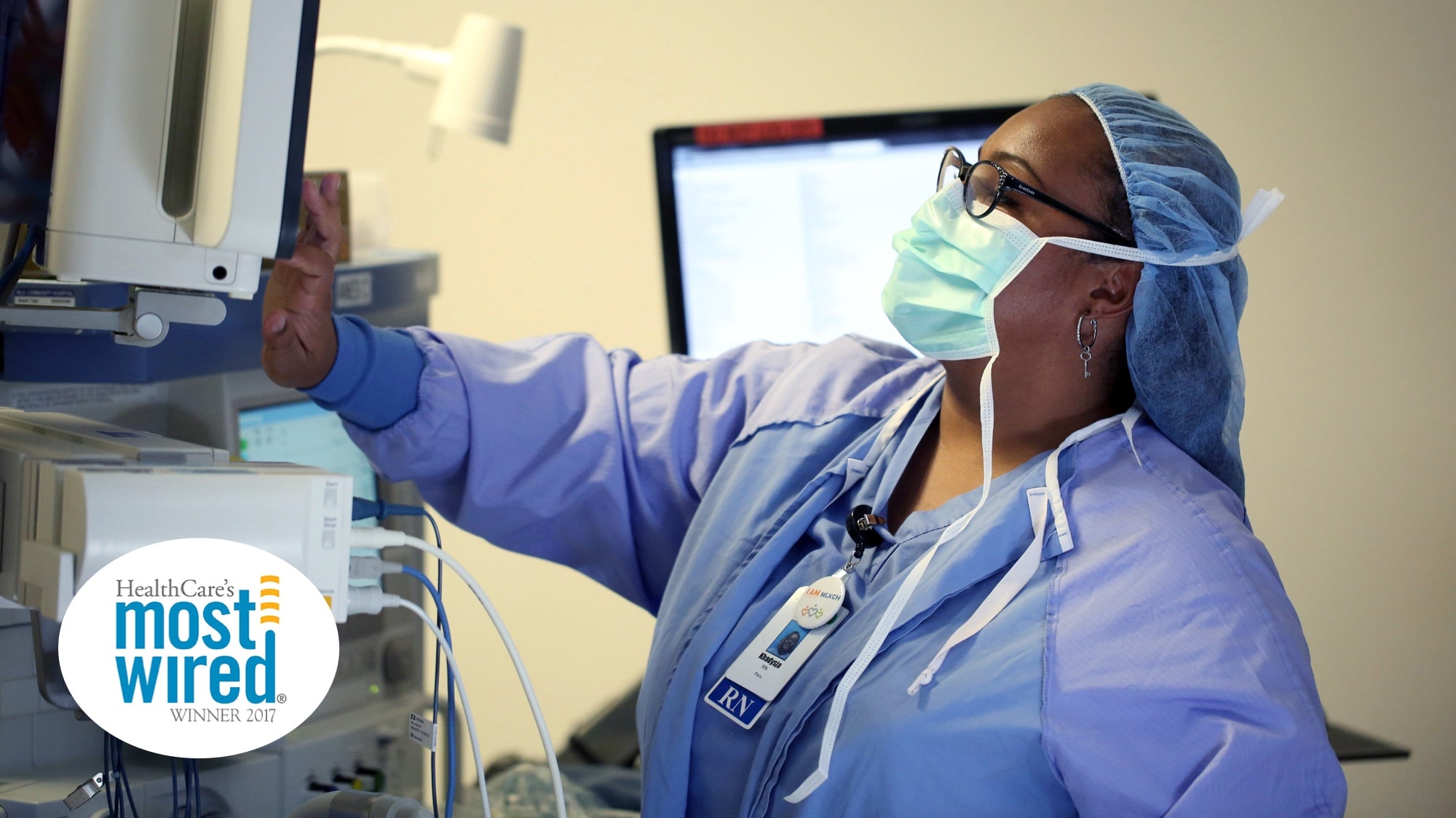 Black female nurse in blue scrubs using medical equipment with logo that reads HealthCare's most wired winner 2017