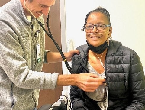 Older African American woman sitting with a white male doctor holding a stethiscope up to her chest