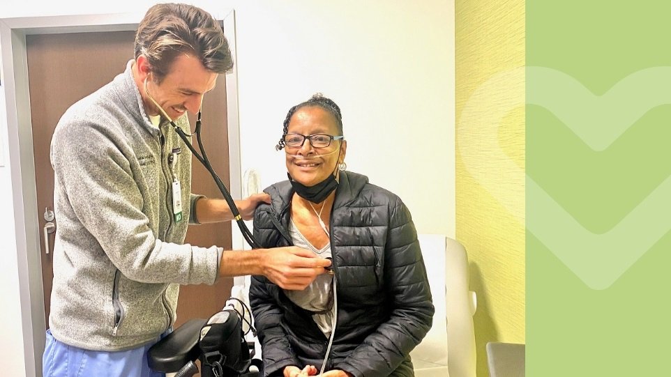 Older African American woman sitting with a white male doctor holding a stethiscope up to her chest