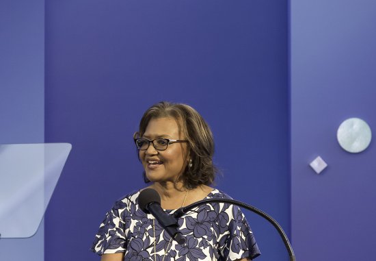 Dr. Elaine Batchlor, a middle-aged Black woman, speaking at a podium at the Dream Lunch