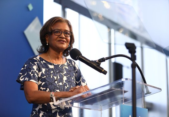 Dr. Elaine Batchlor, a middle-aged Black woman, speaking at a podium at the Dream Lunch