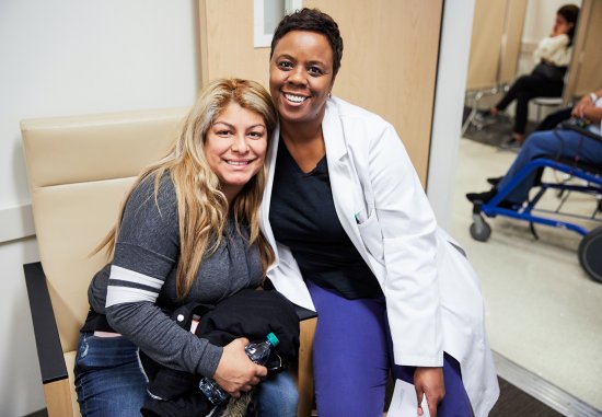 Black female nurse sitting side by side with female patient smiling