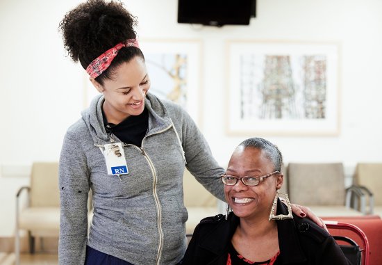 Young Black female nurse smiling down at seated Black female patient