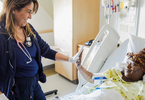 Female nurse sharing a high five with Black female patient lying in hospital bed