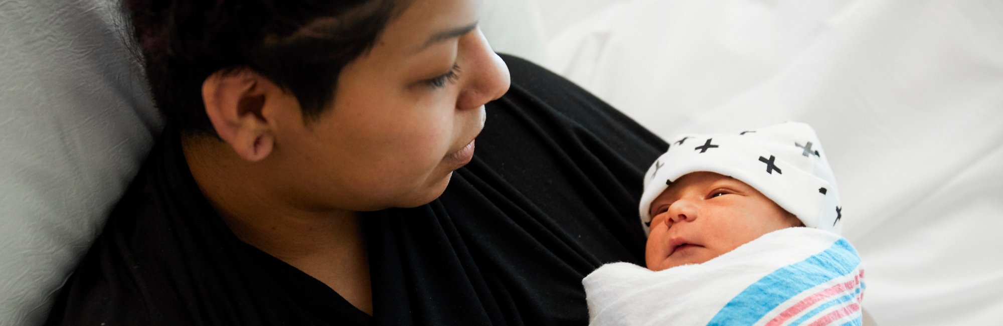 Smiling Latina mom holding and looking at her newborn baby wrapped in a blanket