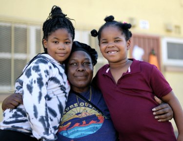 older seated black woman hugging two young black girls 