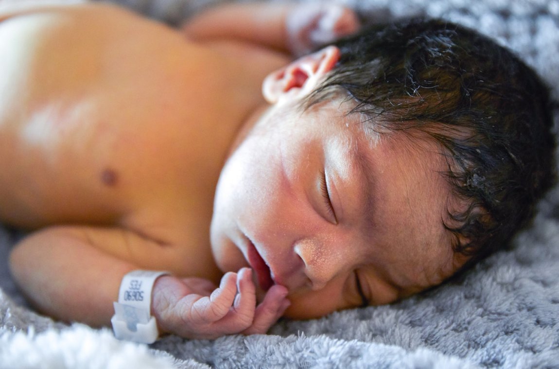 Newborn baby with black hair wearing a hospital id bracelet