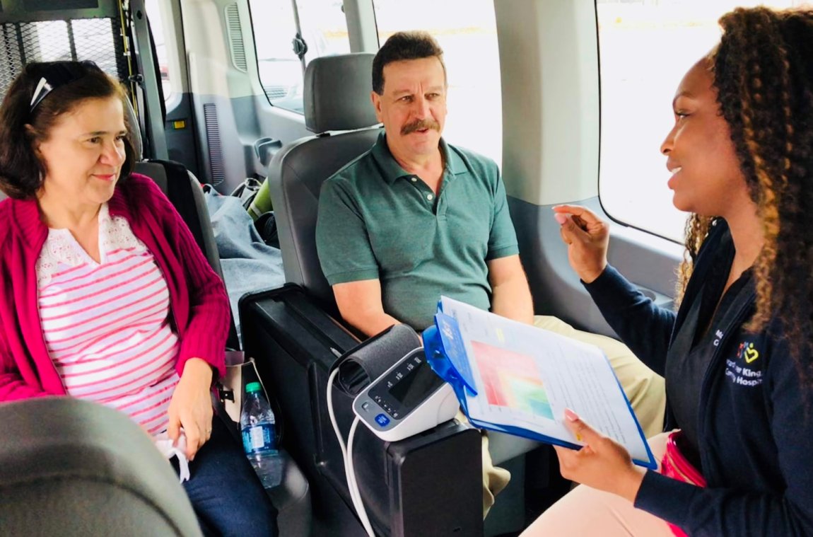 A woman and man, seated in a van, speaking with a hospital representative