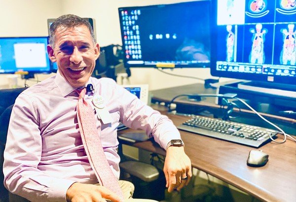 Photo of Dr. Edward Zaragoza sitting at desk smiling next to computer screens