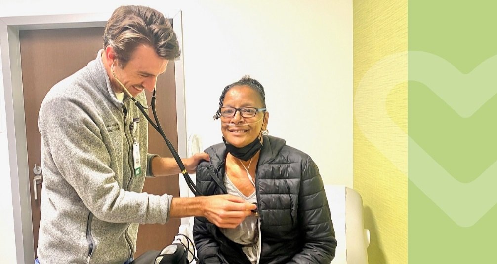 Older African American woman sitting with a white male doctor holding a stethiscope up to her chest