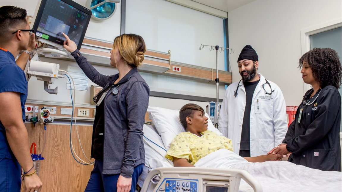 Four doctors and nurses monitoring equipment and speaking to black female patient in hospital bed