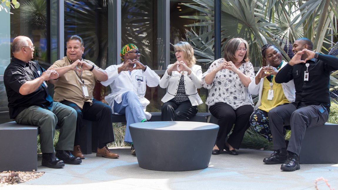 Group of seven staff members making heart gestures with hands and smiling