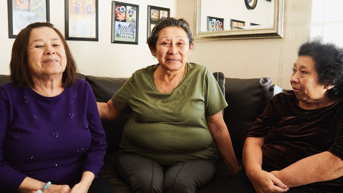 Three older Latina sisters sitting together on couch