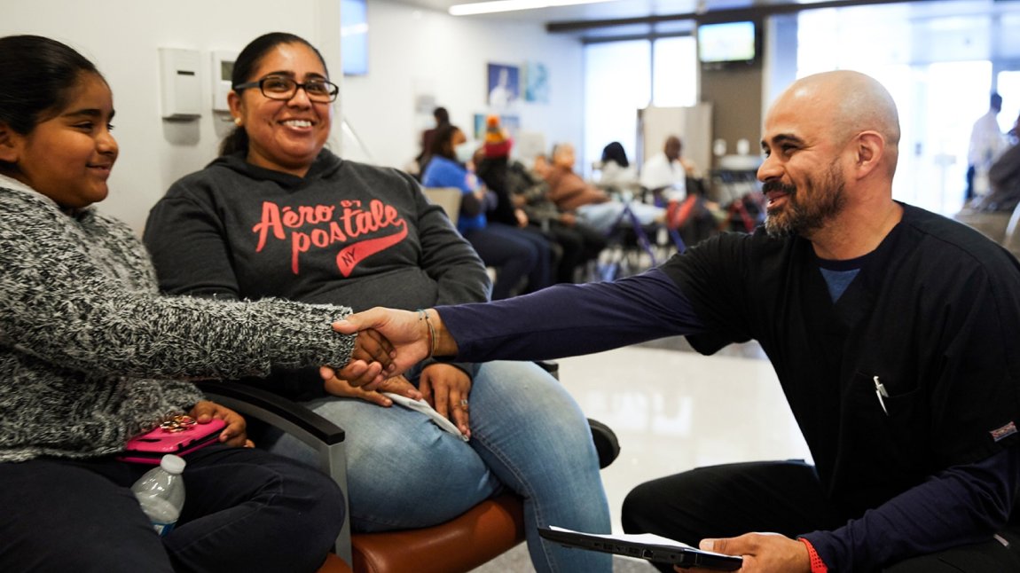 Latino doctor reaching out to hold hands with young Latina patient in Emergency Room waiting room