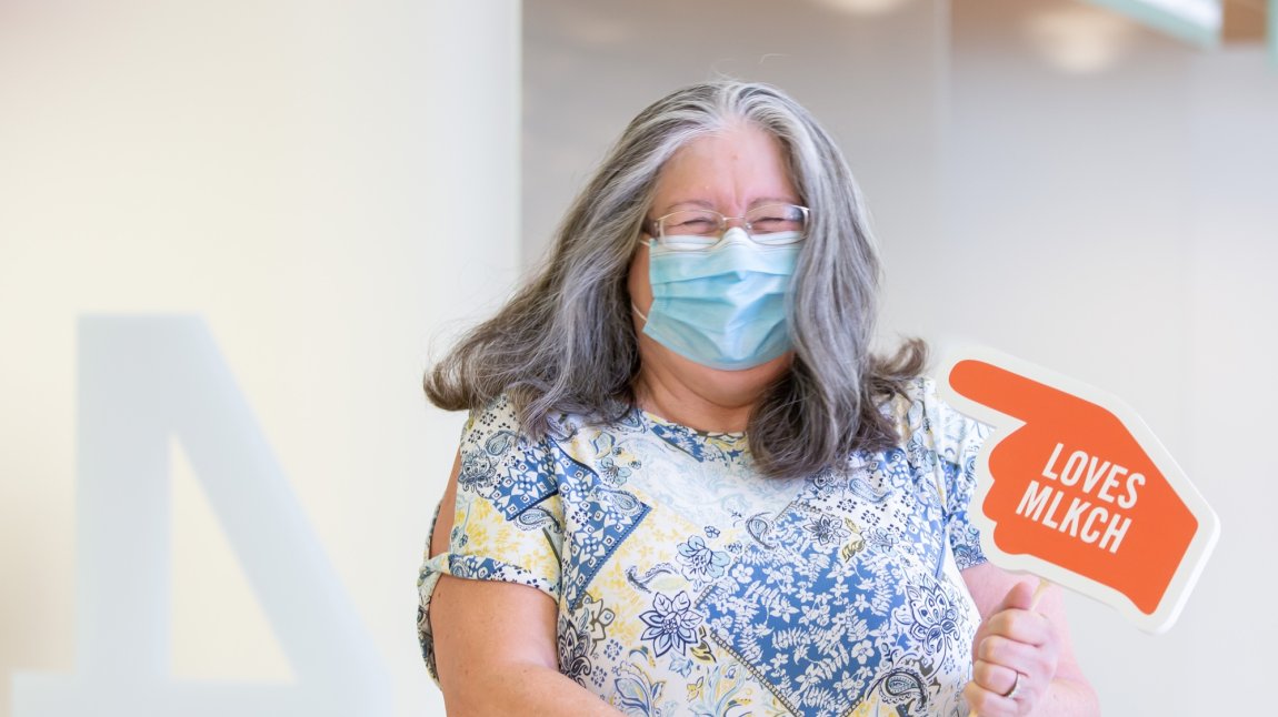 Masked older white woman holding a sign that says loves MLKCH