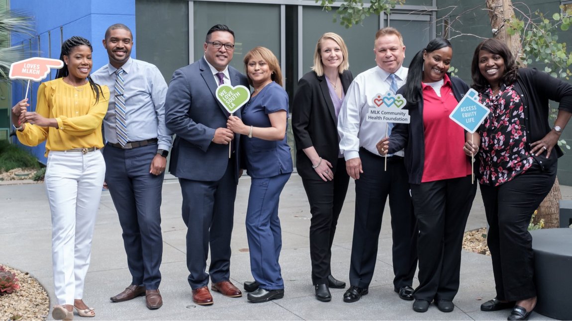 Gorup of eight MLKCH staff members smiling and holding signs that read we love South LA and access equity life