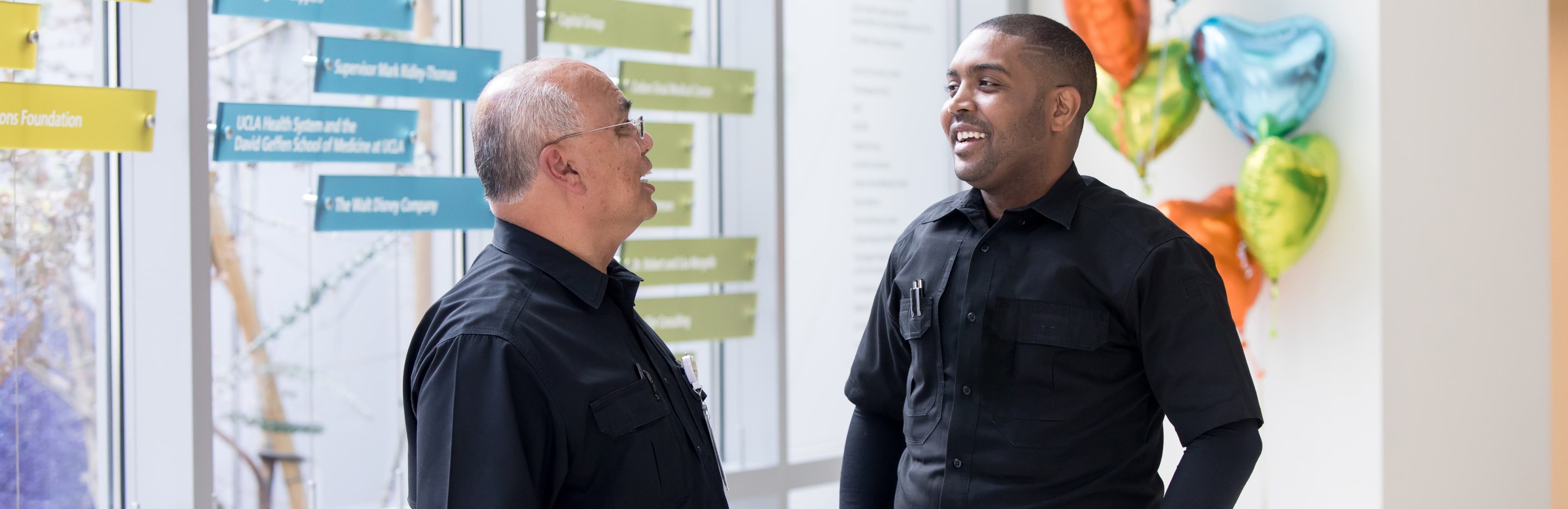 Older male Latino staff member talking and laughing with young Black male staff member