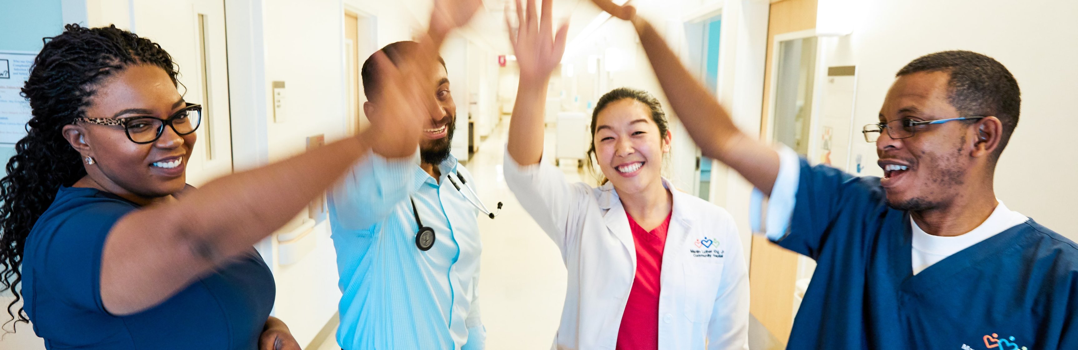 Un grupo diverso de cuatro médicos y enfermeros sonriendo y chocando los cinco