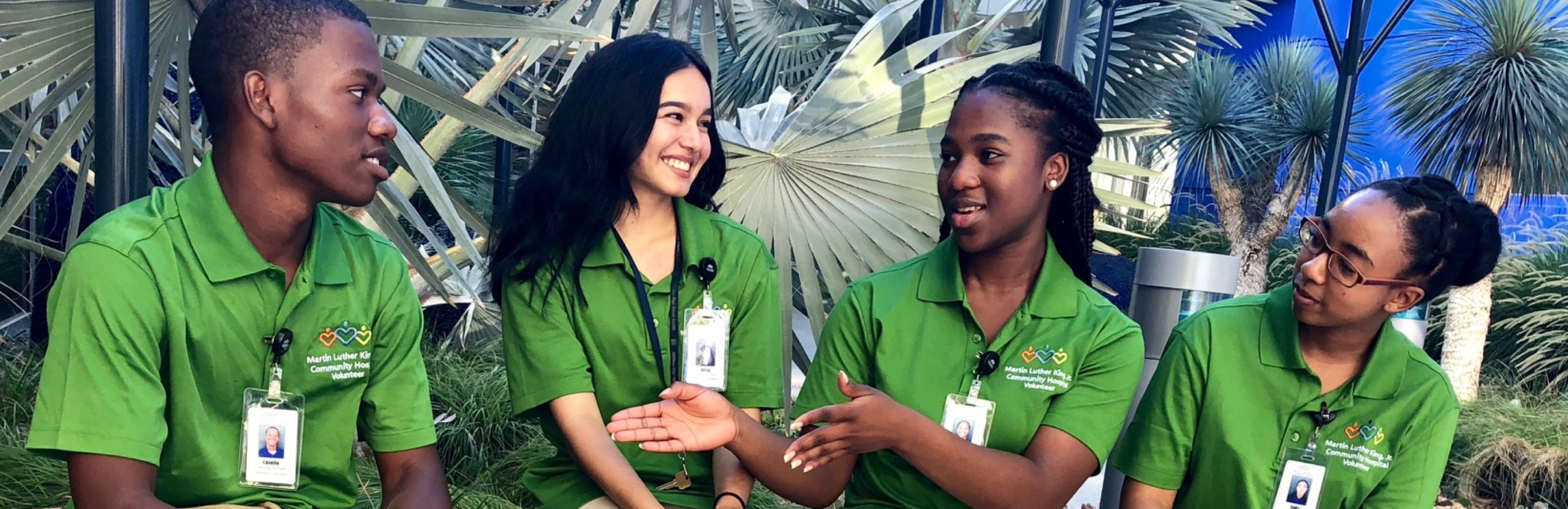 Four high school volunteers wearing green t-shirts sitting next to each other talking