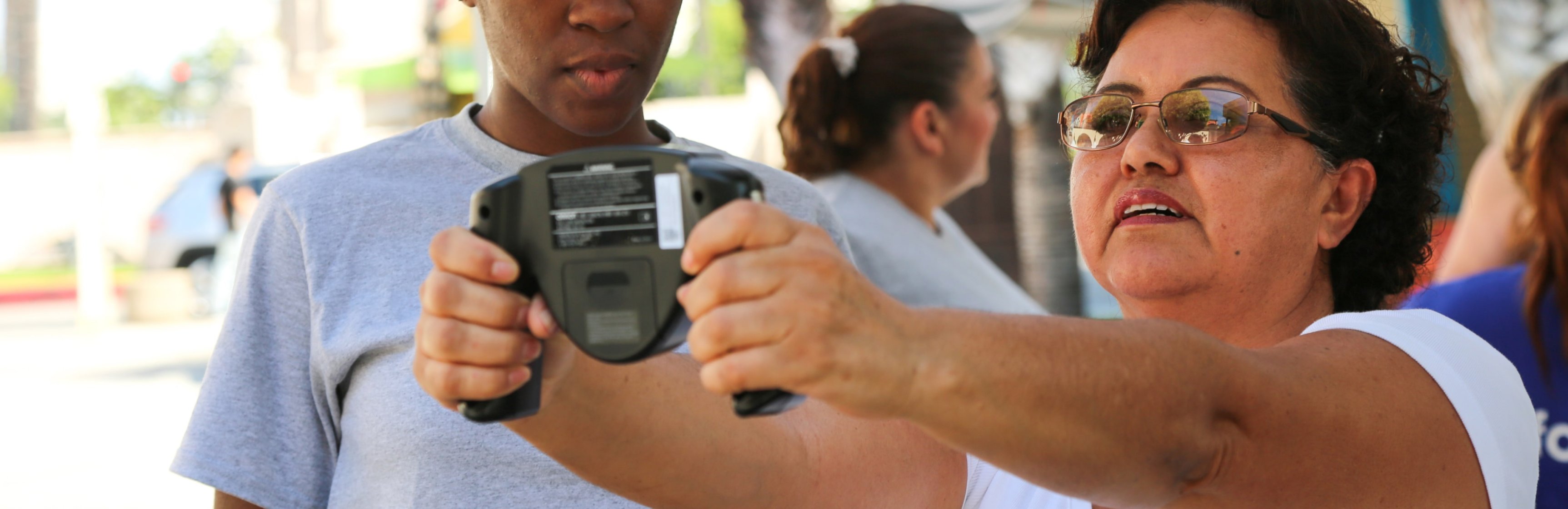 Female Latina patient holds up medical device at outdoor health screening event